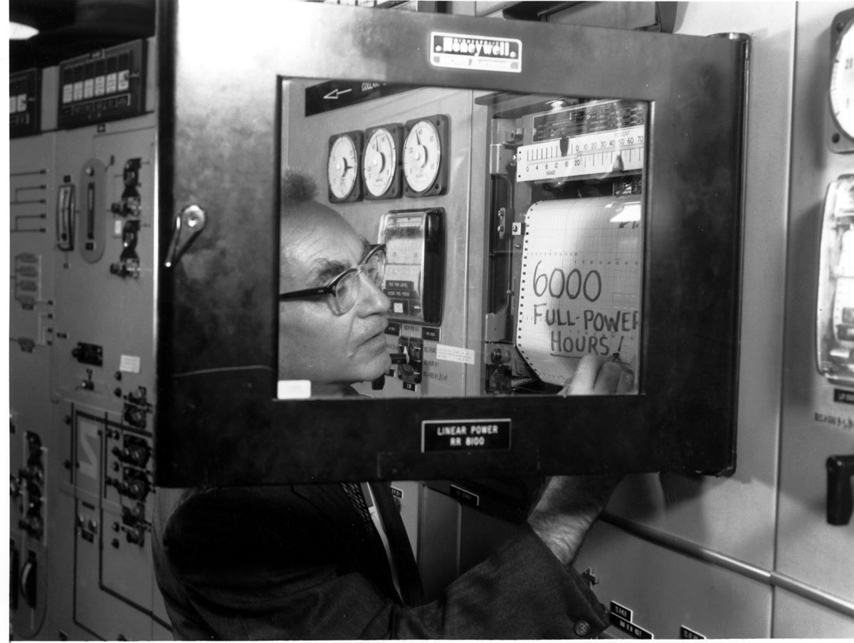 Alvin Weinberg looking through the control room window of the Molten-Salt Reactor Experiment at Oak Ridge National Laboratory, with 6000 full power hours written on the glass.